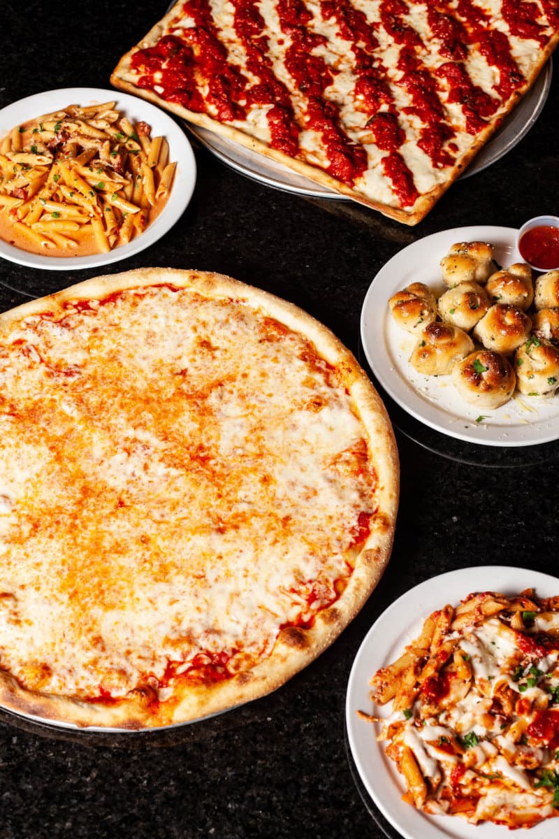 Overhead spread of pizza, pasta, garlic knots on table