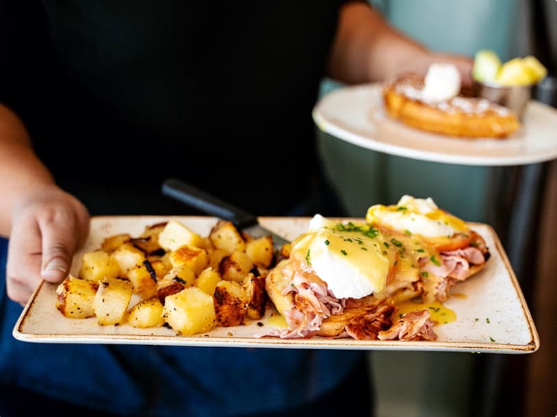 Server holding plate of eggs benedict and potatoes