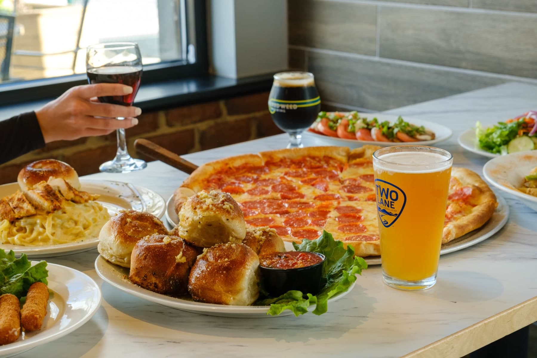 Pepperoni pizza with beer, garlic knots, pasta on table