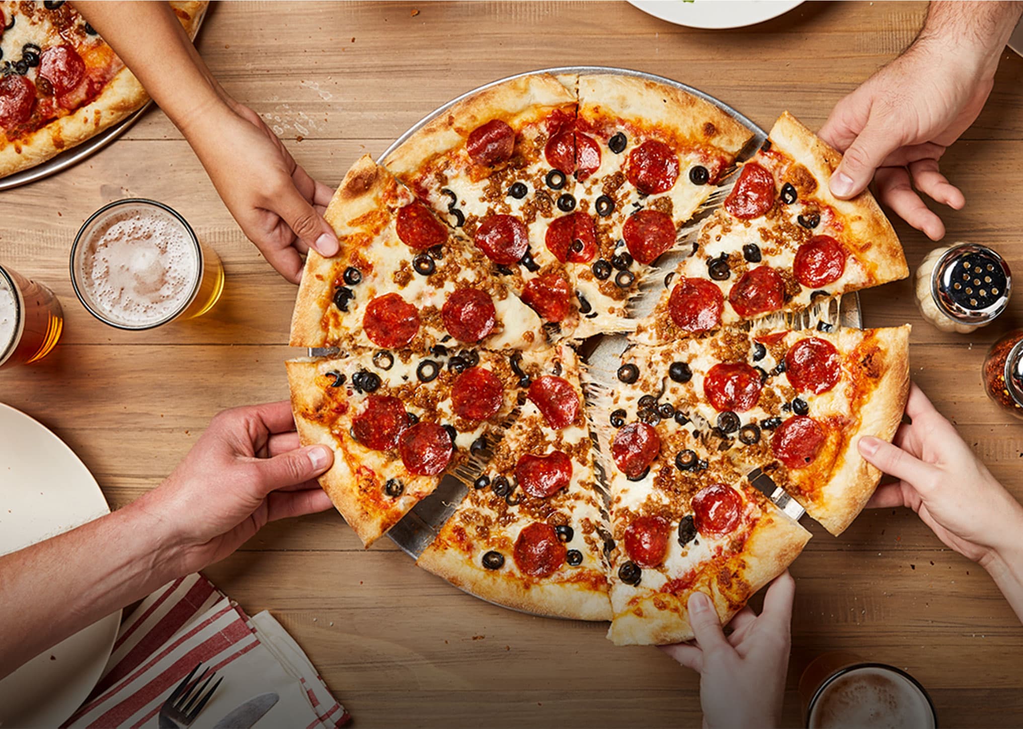 Overhead shot of pepperoni pizza with hands taking slices