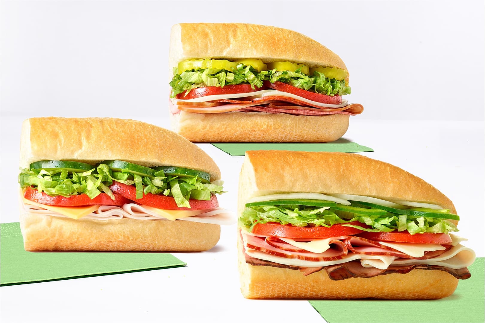 Three deli sandwiches with lettuce, tomato, meats and cheese