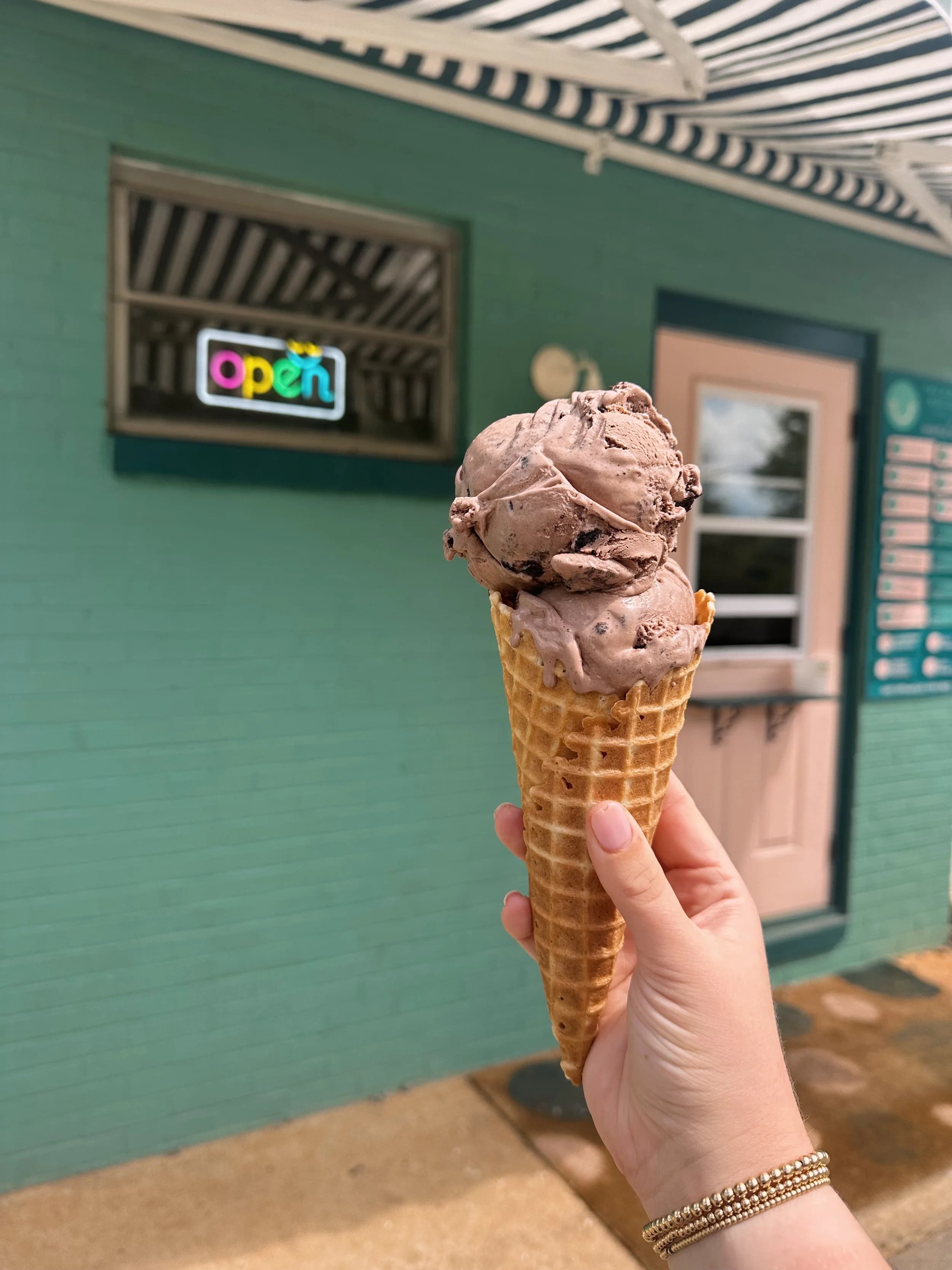 Ice cream cone held outside storefront with open sign