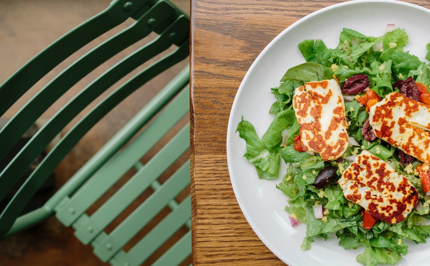 Halloumi salad with olives and greens on white plate