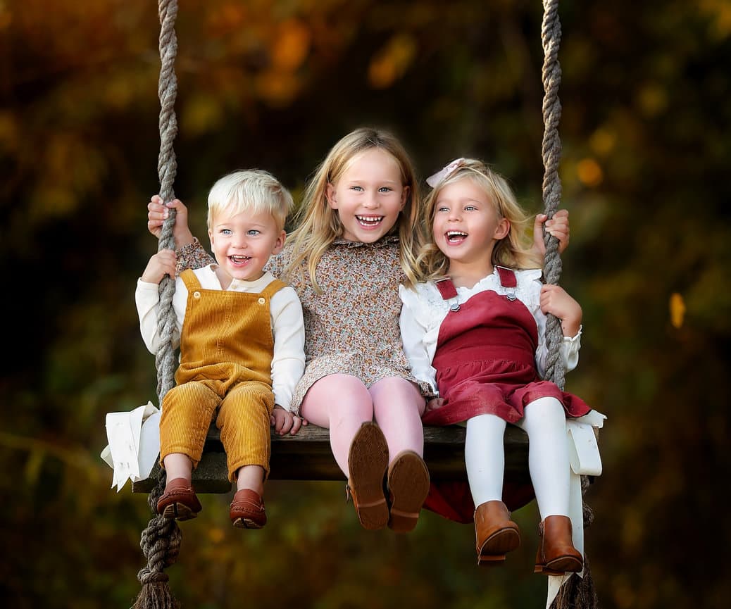 Three children posing on swing outdoors