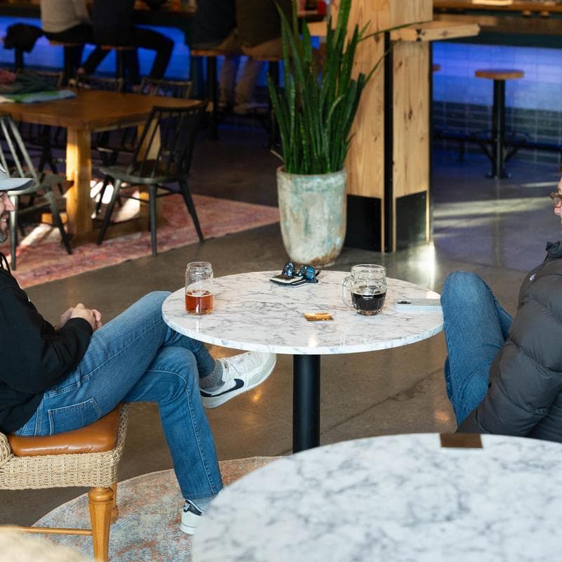 Two people at marble tables with drinks in taproom