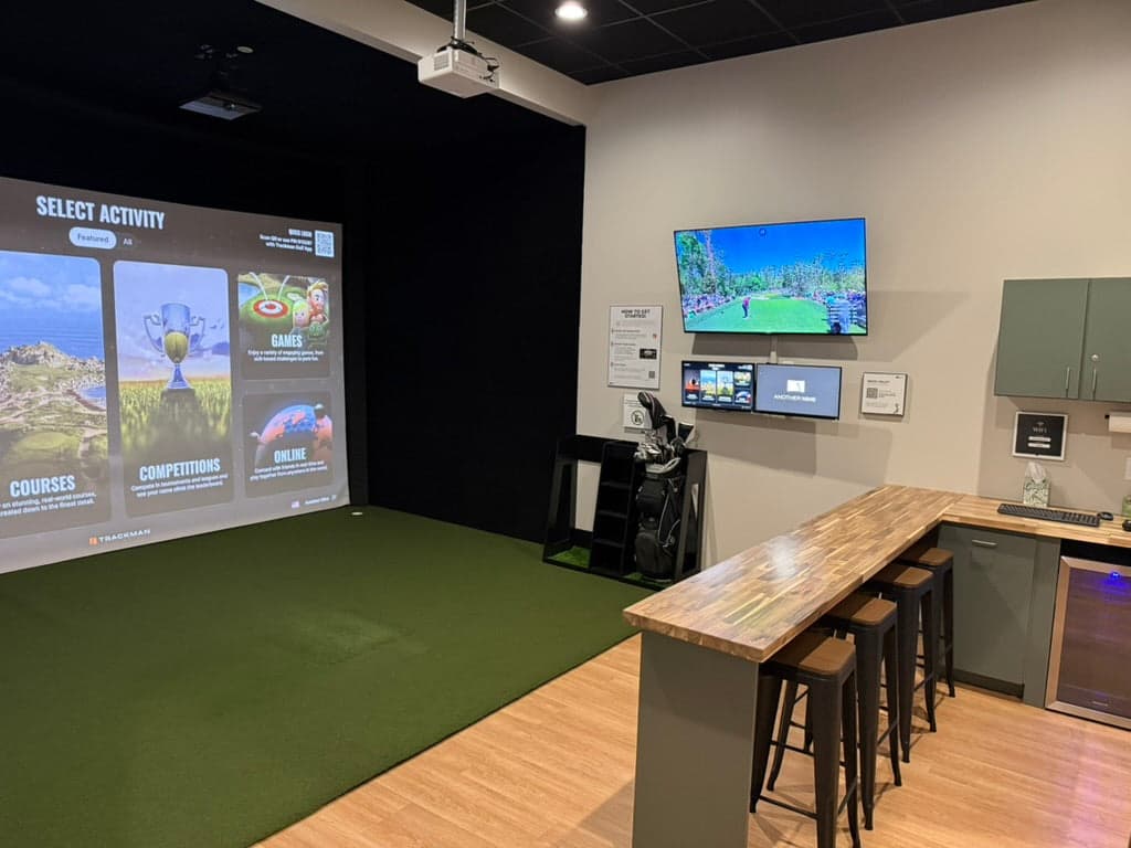 Golf simulator room with screen, bar and TVs