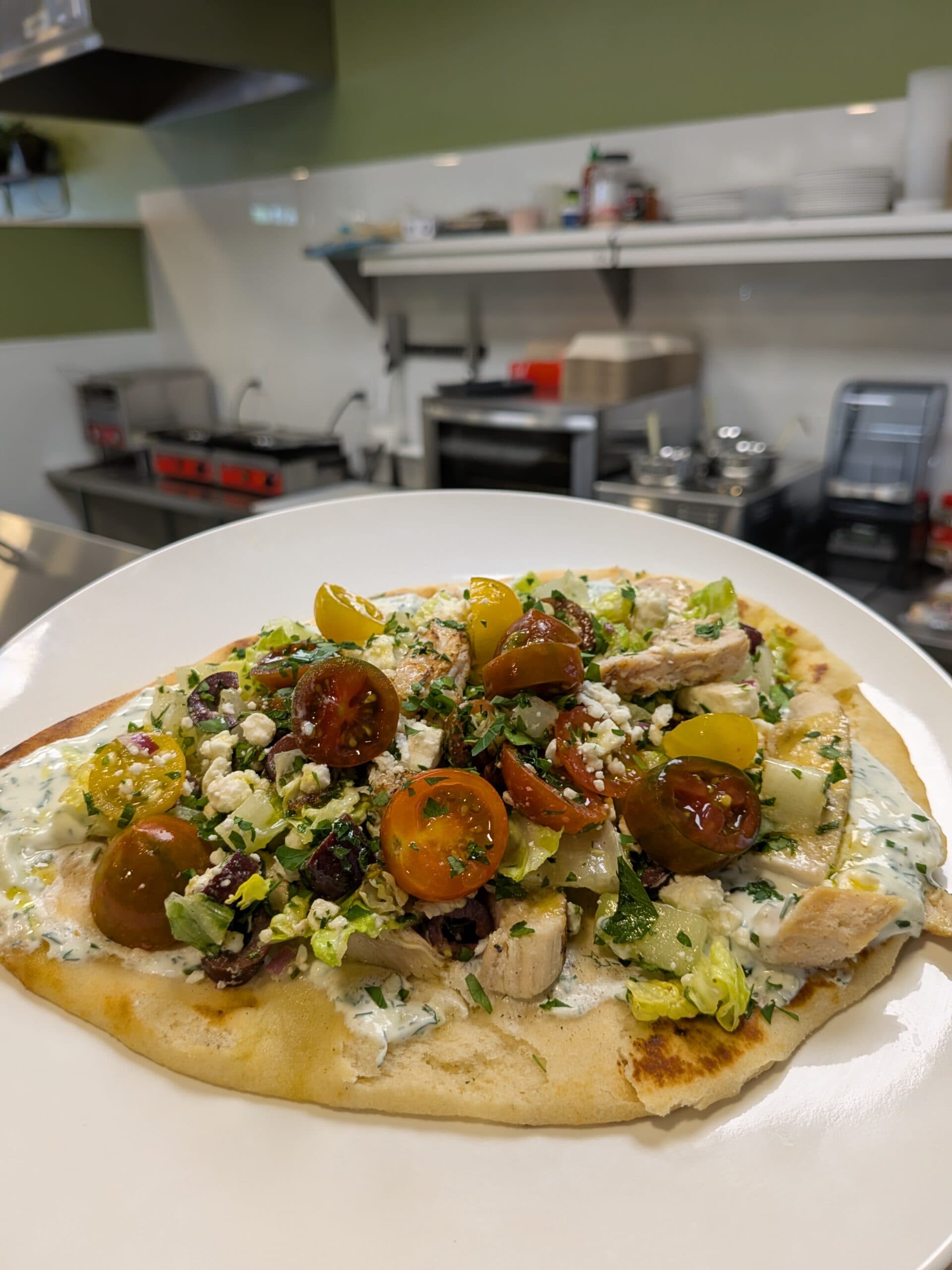 Greek chicken flatbread pizza on white plate in kitchen