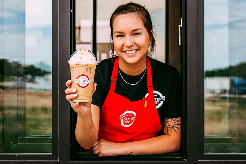 Barista at drive-thru window holding iced coffee drink